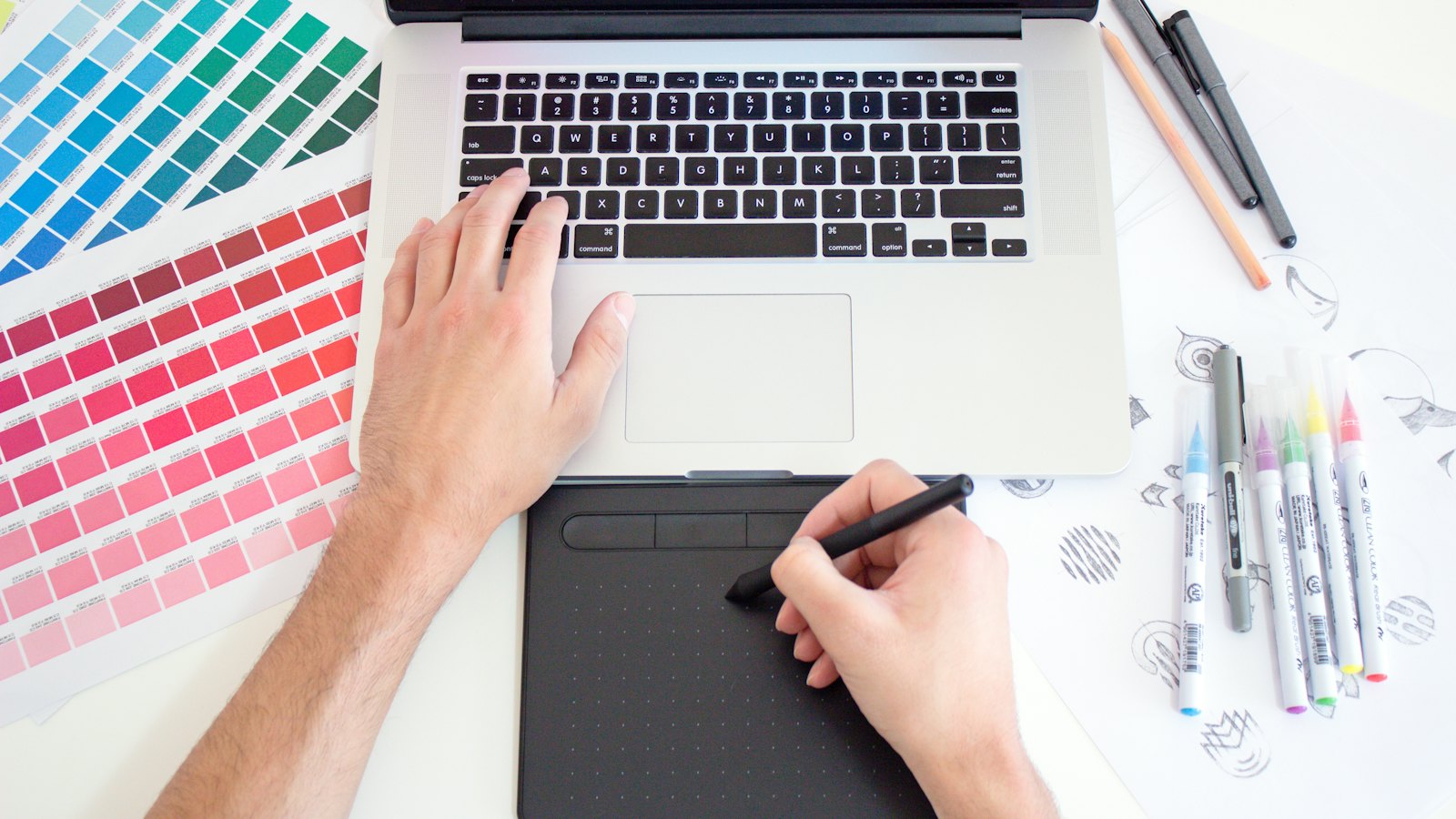 Designer sketching a brand identity next to colour swatches and a laptop