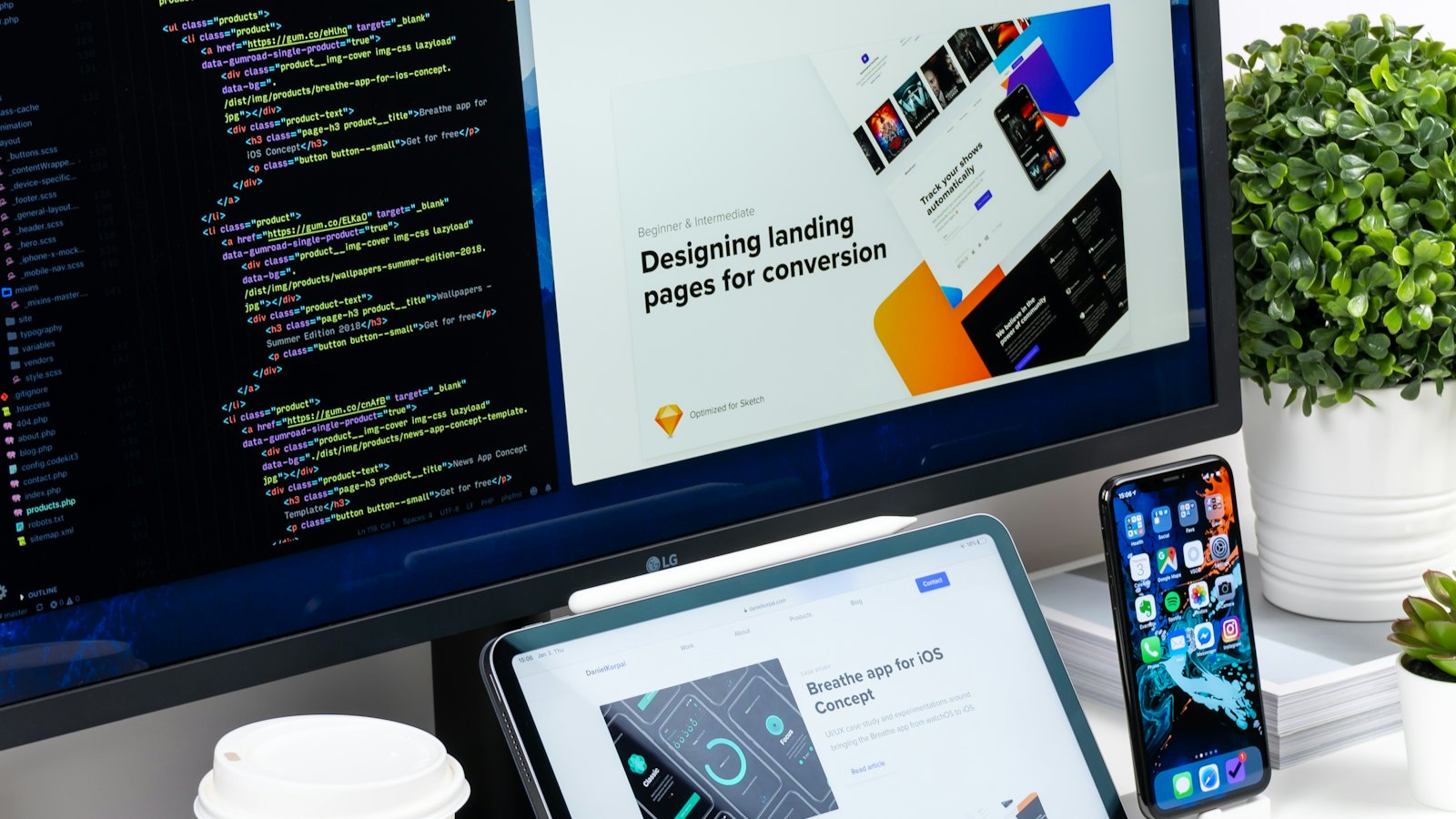 Website code on a monitor beside responsive web page designs on a tablet and phone